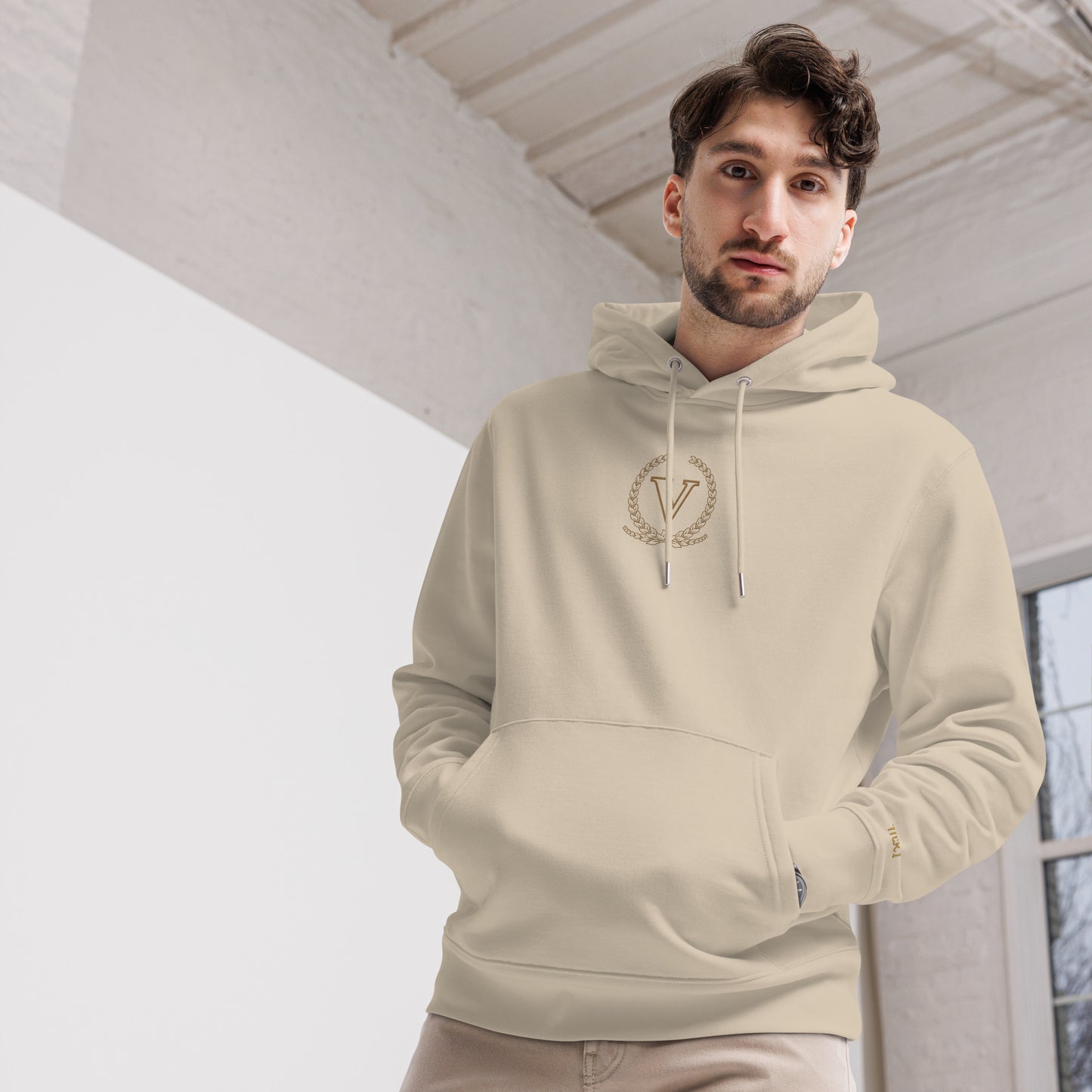 Man wearing a beige hoodie with a logo indoors